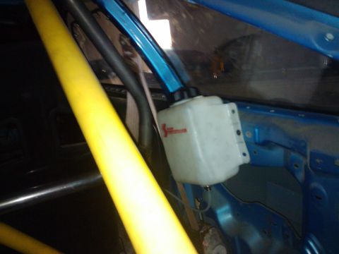 1995 Ford Probe - The interior of a car shows a yellow roll cage and a white fluid reservoir mounted to blue metal framing.