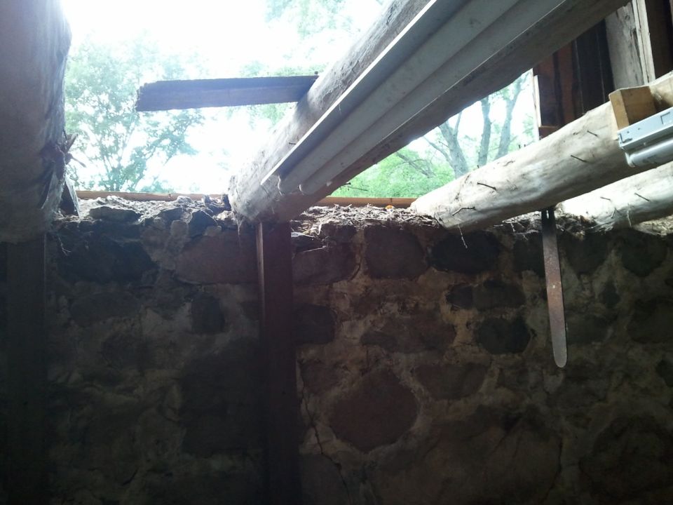 Inside a stone building with rough wooden beams overhead and an opening to the outside