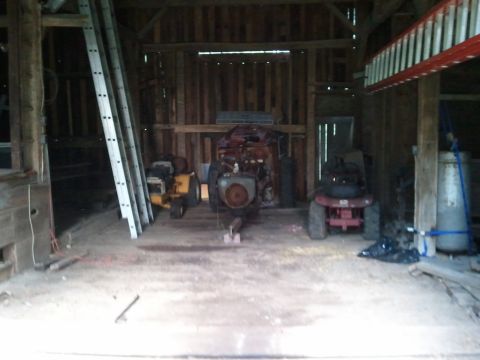 1985 Ford F-150 - Several riding lawn mowers are stored inside a rustic barn with ladders and ladders.