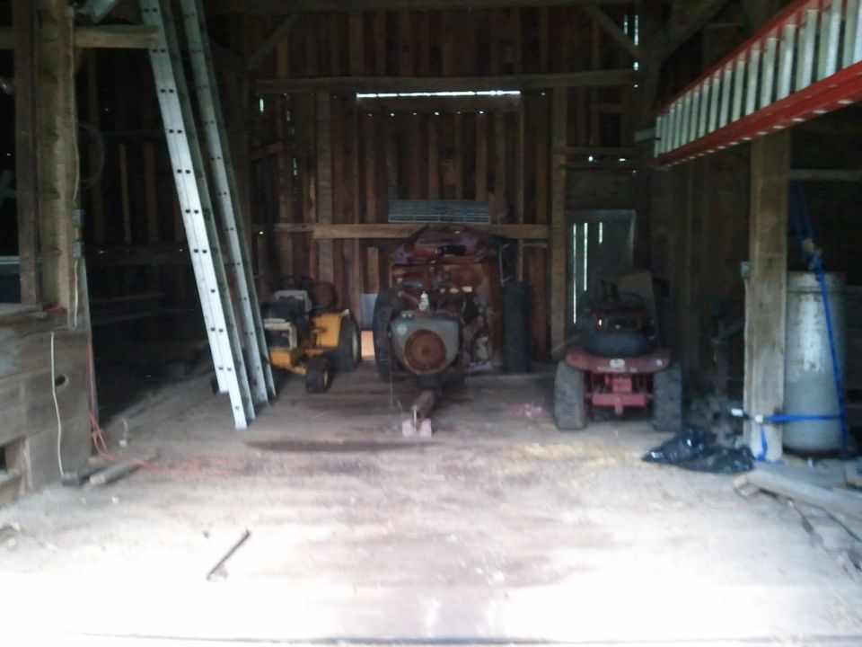 Three riding lawn mowers inside a wooden barn, one yellow, one red, and one red with a large engine