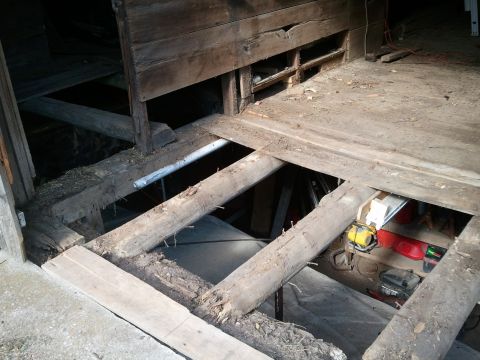 1985 Ford F-150 - The interior of a decaying wooden structure shows significant damage to its floor and support beams.