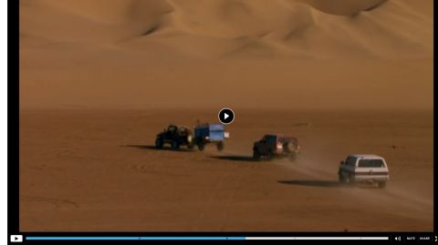 1994 Ford Bronco - Multiple off-road vehicles traverse a sandy desert terrain under a clear sky.