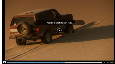 1994 Ford Bronco - A red Ford Bronco navigates sandy terrain, its spare tire mounted prominently on the rear.