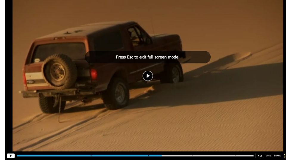 Red Ford Bronco with spare tire on rear door driving on sand dunes