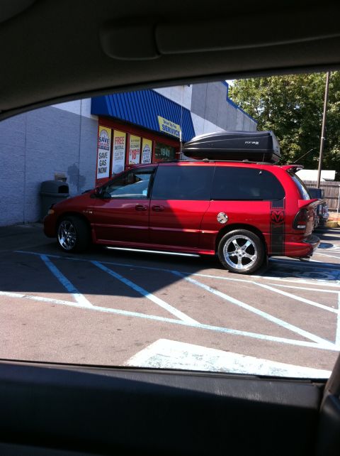 2007 Subaru Impreza - A red minivan with a roof box is parked in a lot outside a building.