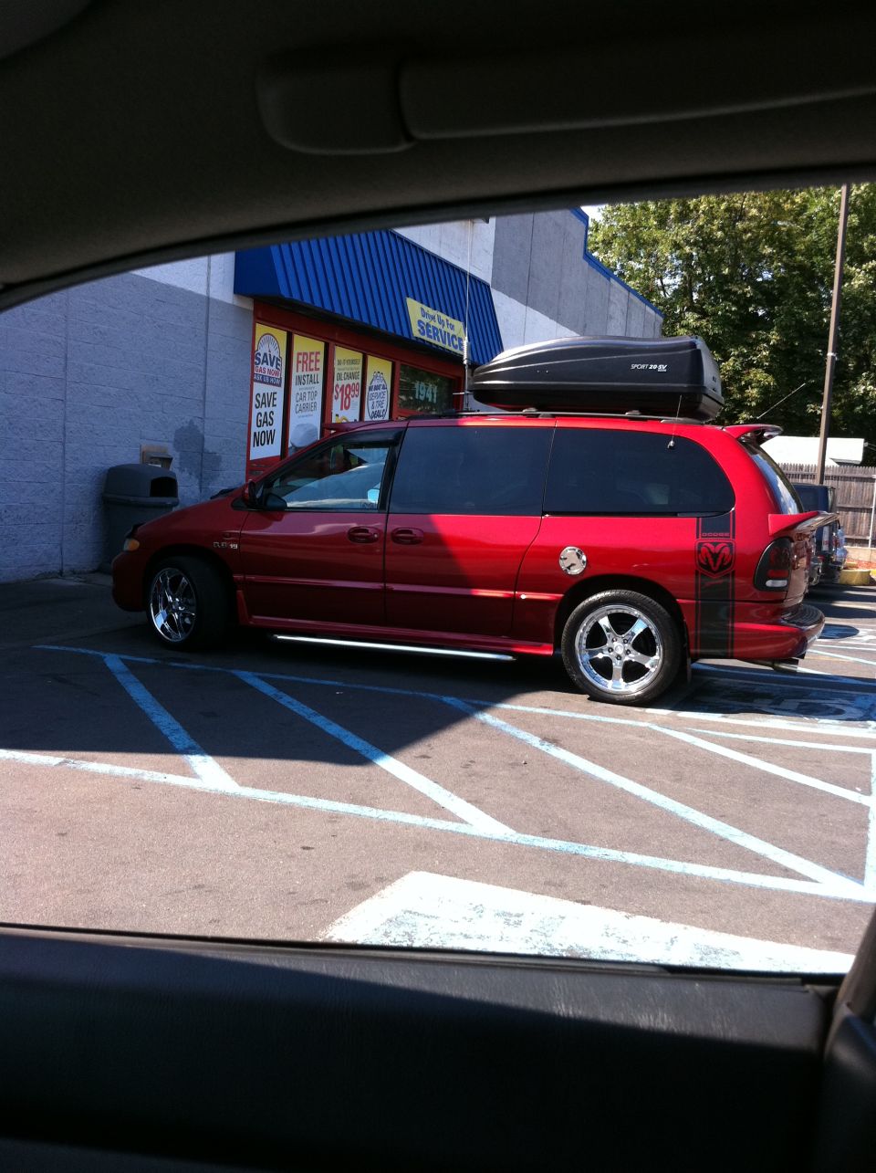Lowered red Dodge Caravan with chrome wheels, Ram graphics and roof cargo box in store lot