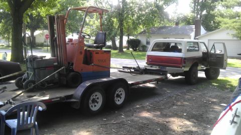 1989 Ford Bronco - A red and white Ford Bronco is being towed on a trailer, with a forklift loaded in front of it.