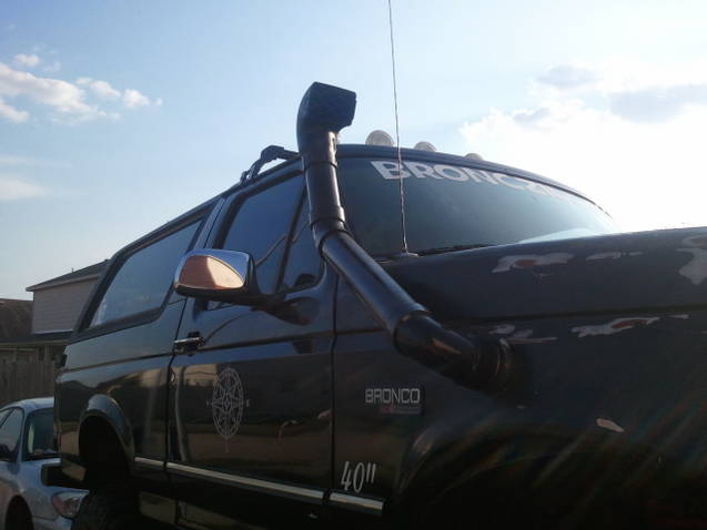 Dark Ford Bronco with snorkel, roof rack, and compass decal on door. "BRONCO" text on windshield