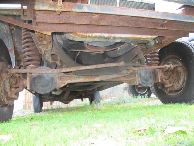 Underside view of a heavily rusted truck frame, suspension, and tires