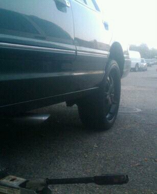 1996 Mercury Grand Marquis - A dark green 1996 Mercury Grand Marquis sedan is viewed from the side, focusing on the rear wheel and lower body.