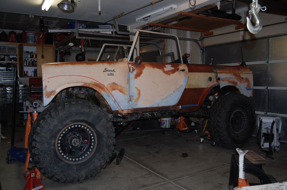 1961 International Scout side view, primer and rust, large tires, in garage