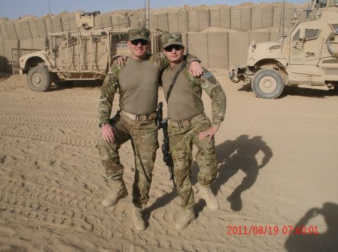 1988 Ford Bronco - Two soldiers stand together in a sandy area, with armored vehicles and fortifications in the background.