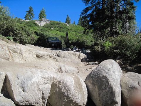 1986 Ford Bronco - A dark SUV tackles a challenging rocky terrain on a sunny day.