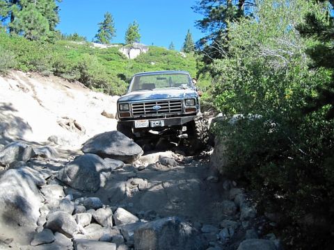 1986 Ford Bronco - This 1980s Ford Bronco tackles a challenging, boulder-strewn path under a clear blue sky.