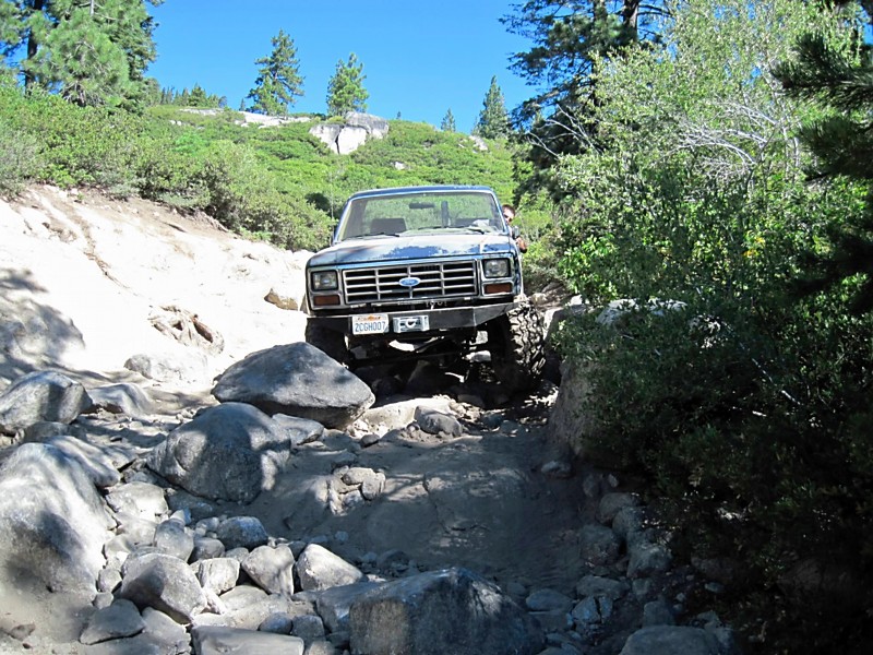 Blue 1980s Ford Bronco navigating a rocky off-road trail