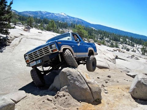 1986 Ford Bronco - This modified Ford Bronco is navigating a rocky off-road course with a clear blue sky above.