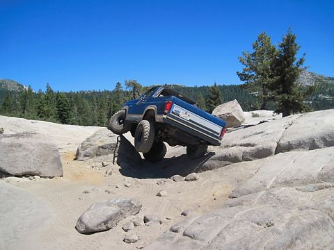 1986 Ford Bronco - Blue 1986 Ford Bronco navigating a rocky off-road course under a clear blue sky.