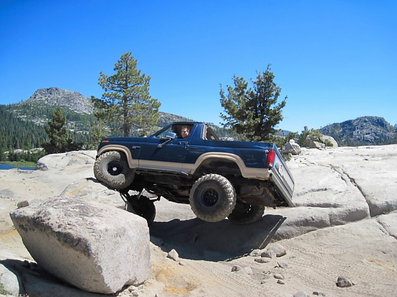 Blue off-road SUV with lifted suspension driving over rocks