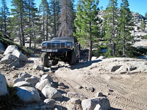 1986 Ford Bronco - This lifted 1980s Ford Bronco navigates a challenging, rocky off-road path through a forest.