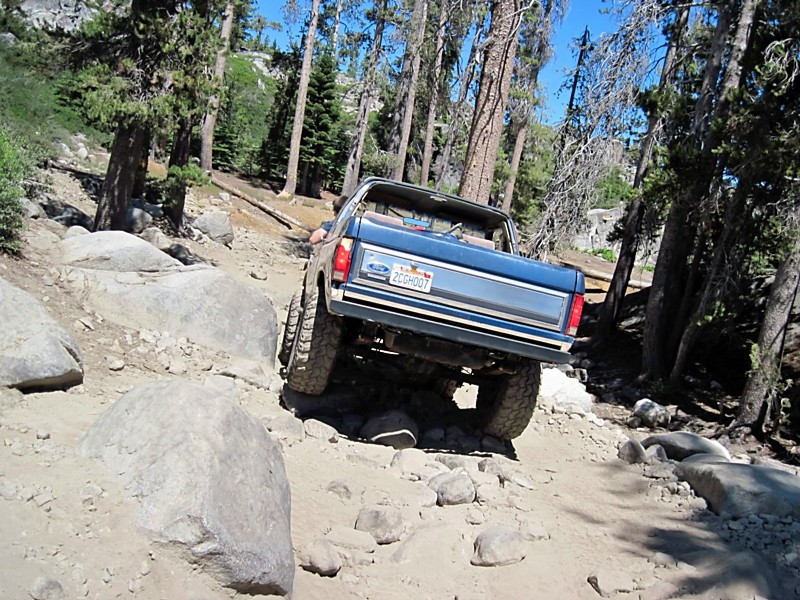 1986 Ford Bronco navigating a boulder-strewn mountain path, rear view