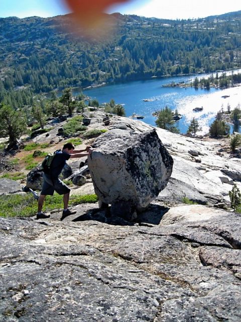 1986 Ford Bronco - Man attempts to move a large boulder on a rocky terrain overlooking a scenic lake and forest.