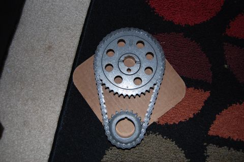 1994 Ford Bronco - A new double-roller timing chain set laid out on a cardboard scrap over a black and red patterned rug, with the multi-keyway cam sprocket a…