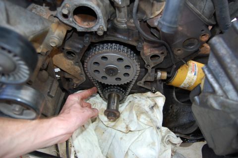 1994 Ford Bronco - A hand reaches into an engine bay to point at the timing chain and camshaft sprocket on an engine with the timing cover removed, the cranks…