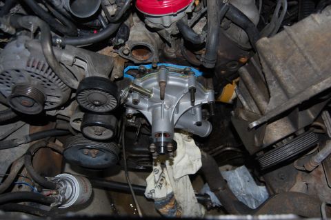 1994 Ford Bronco - Close-up of a newly installed silver water pump on an engine block, with the accessory drive belt tensioner pulleys, alternator, and variou…