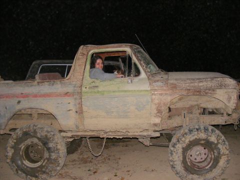 1978 Ford Bronco - A woman sits in the driver's seat of a heavily muddied 1978 Ford Bronco.