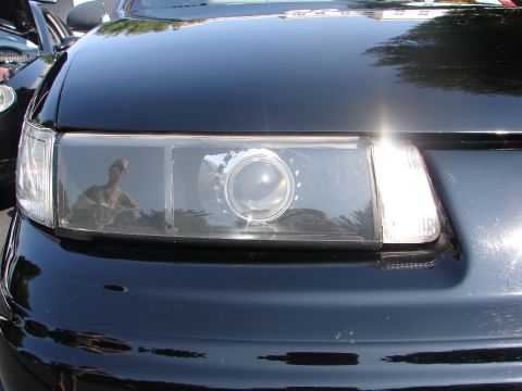 1992 Ford Taurus - A reflection of a person is visible in the clear lens of a car's headlight assembly.
