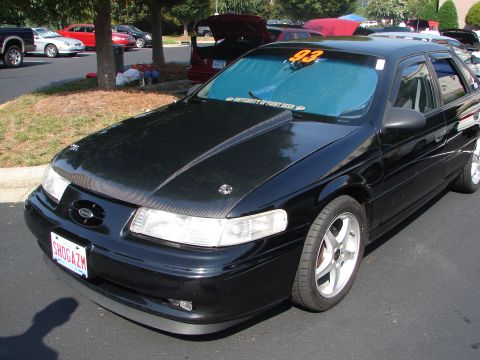 1992 Ford Taurus - A black sedan, possibly a 1992 Ford Taurus, is parked outdoors with other vehicles in the background.