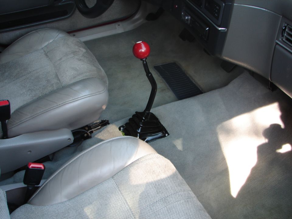 Car interior showing light grey seats and a black shifter with a red knob