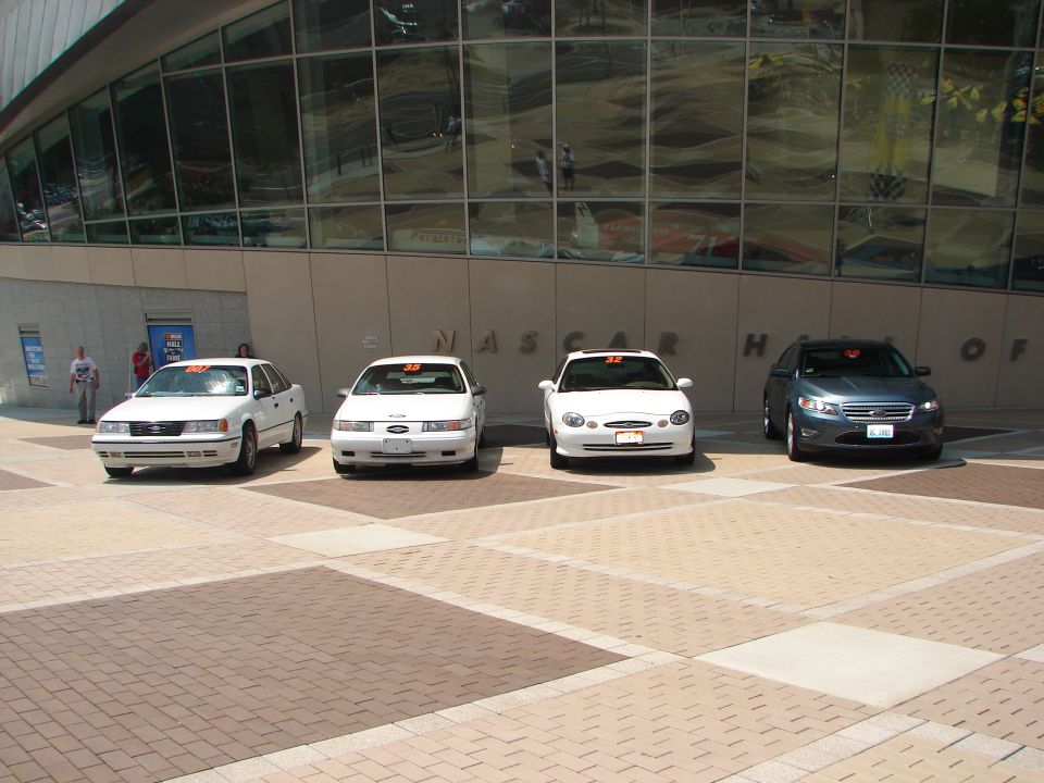 Four white and blue cars parked in front of NASCAR Hall of Fame