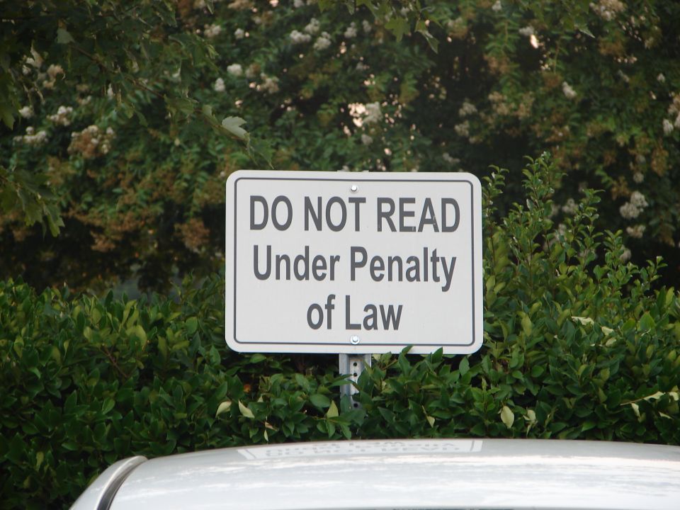 Sign says 'DO NOT READ Under Penalty of Law'. Some bushes and a car roof are visible