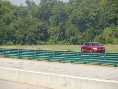1992 Ford Taurus - A red sedan, possibly a Ford Fusion, is seen on a racetrack with green guardrails in the foreground.