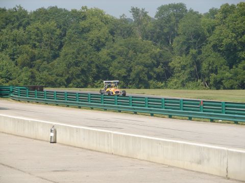 1992 Ford Taurus - An open-wheel race car speeds around a track bordered by green guardrails and trees.