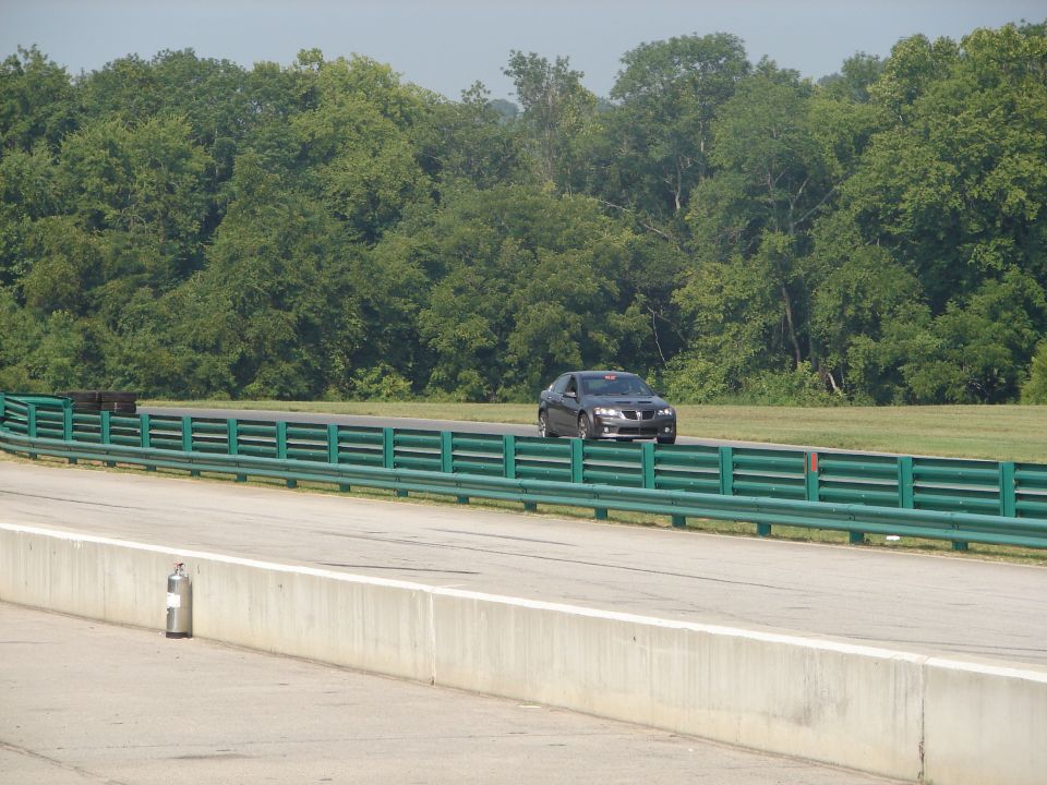 Dark sedan on racetrack, trees in background