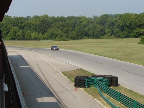 1992 Ford Taurus - A dark sedan is seen on a racetrack, with trees and grass in the background.