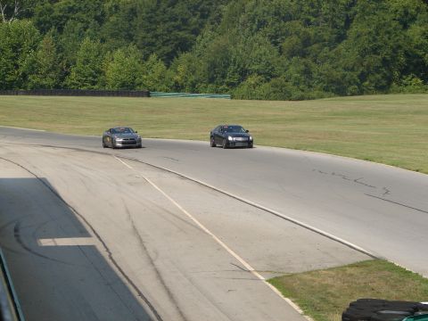 1992 Ford Taurus - Two cars are on a race track during a sunny day, with a wooded area and grassy field visible.