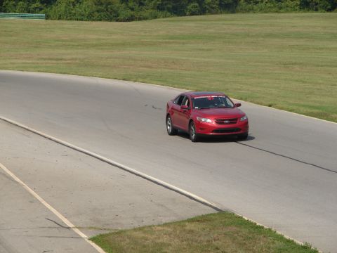 1992 Ford Taurus - A red sedan drives on a race track under a clear sky.
