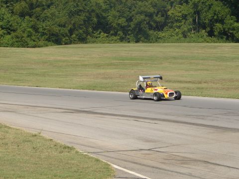 1992 Ford Taurus - A yellow race car with a spoiler is seen on a paved track with grassy areas and trees in the background.