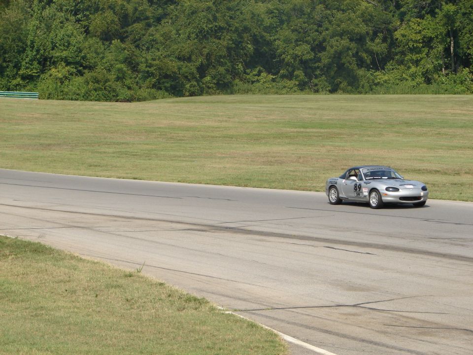Silver convertible sports car with number 69 on the side, driving on a race track with trees and grass in the background