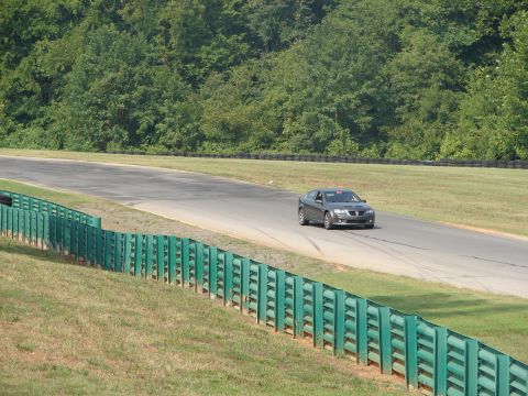 1992 Ford Taurus - Gray sedan navigates a turn on a racetrack, with a green safety fence in the foreground and trees in the background. Watermark visible.