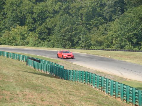 1992 Ford Taurus - Red sports car navigates a turn on a paved race track with a wooded background.