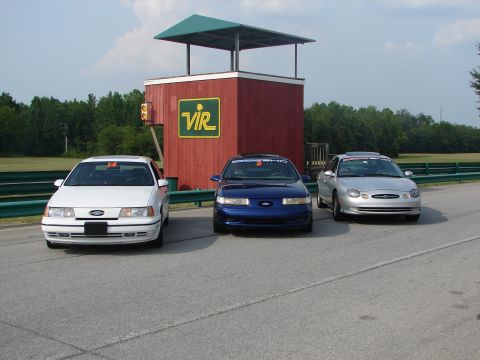 1992 Ford Taurus - Three Ford Taurus sedans, including a white 1992 model, are parked on a racetrack in front of a building.