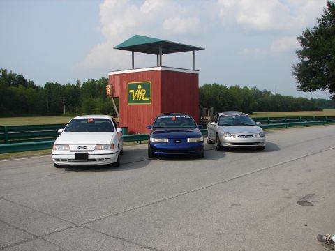 1992 Ford Taurus - Three Ford Taurus sedans are lined up on a racetrack, with a red observation tower in the background.