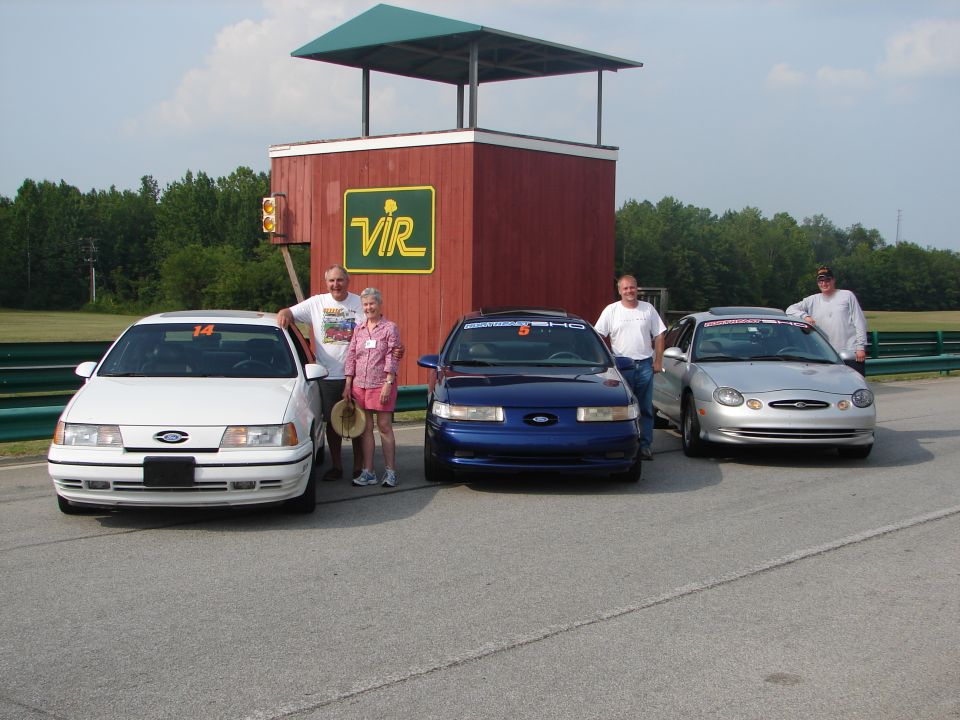 White 1992 Ford Taurus, blue 1992 Ford Taurus, and silver 1992 Ford Taurus parked on asphalt with a red building and green trees in the background