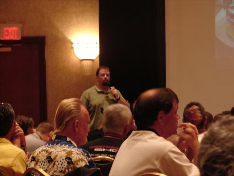 1992 Ford Taurus - A speaker addresses an audience at a convention, with an 'EXIT' sign visible in the background.