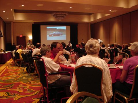 1992 Ford Taurus - A red sedan is displayed on a projection screen during a convention event.