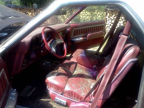 1979 Ford Ranchero - The interior of a vehicle features maroon upholstery with a distinctive patterned design on the seats and a red steering wheel.